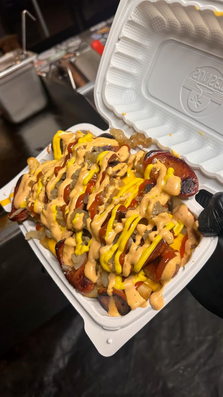 Grilled sausage slices and fries topped with onions, mustard, ketchup, and a creamy sauce.