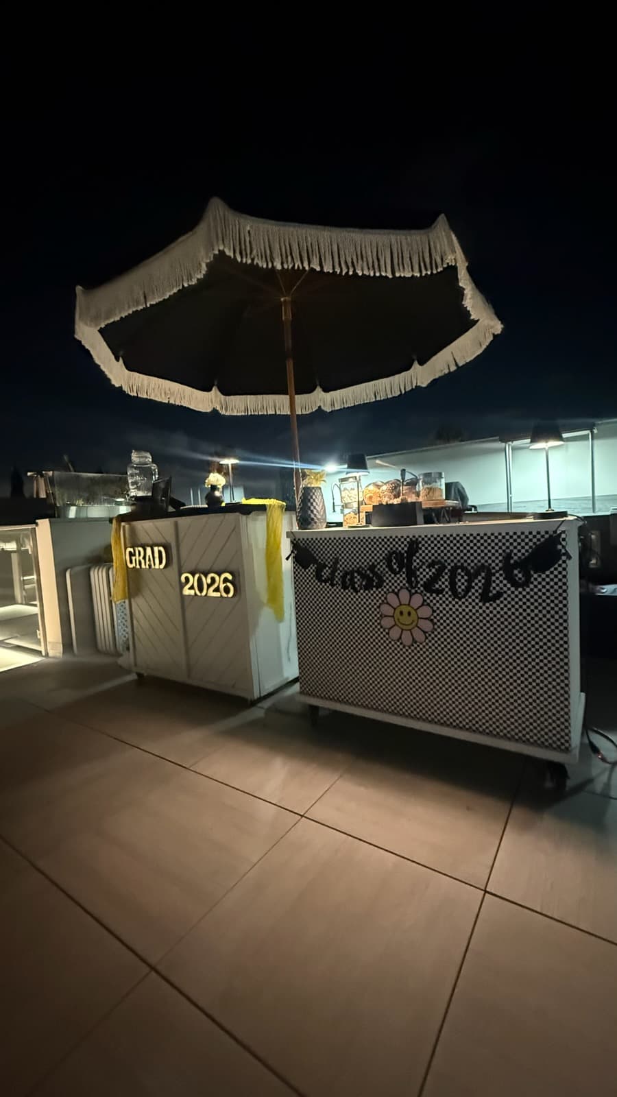 Two mobile bars decorated for a Class of 2026 graduation party under a fringed umbrella.